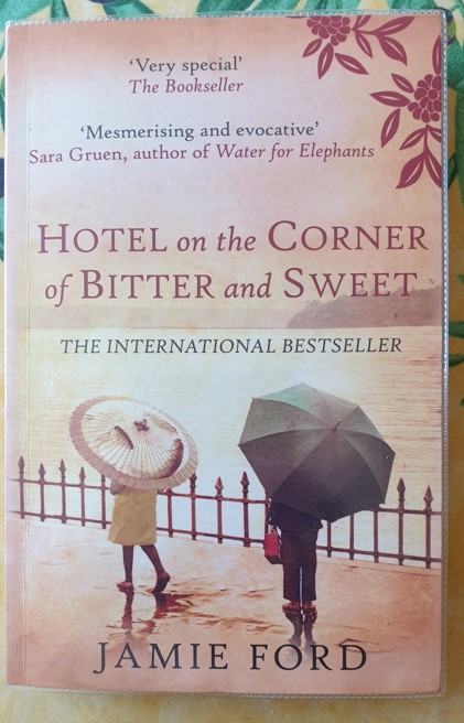 Book cover showing a man and woman with contrasting umbrellas walking beside water