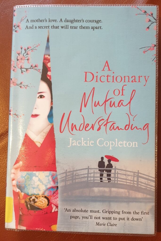 Book cover with two people, one with an umbrella, on a light bridge offset by a Geisha looking through a torn curtain.